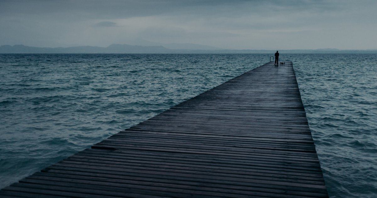 Personne seule au bout d'un long ponton qui s'enfonce dans une mer calme, sous un ciel couvert